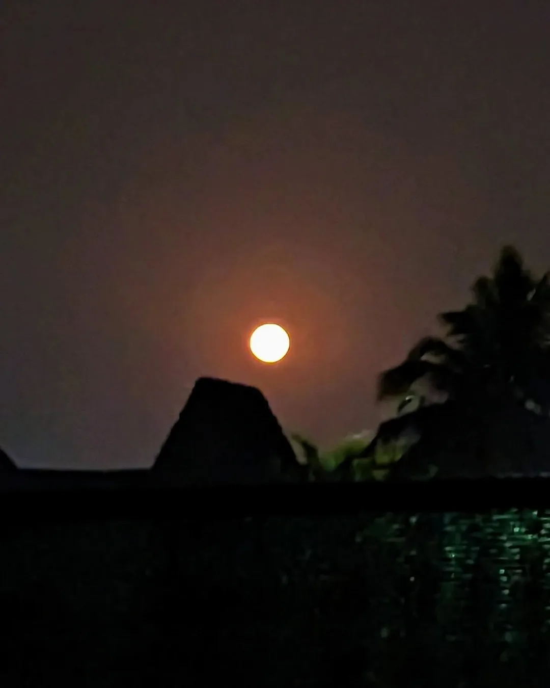 An orange moon rises over a red tiled roof.